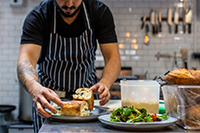A chef plating a sandwich dish in a professional kitchen